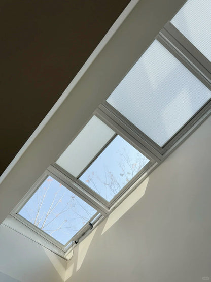 Motorized 1-inch honeycomb skylight blinds with aluminum frame and steel wire tension system installed on a roof window