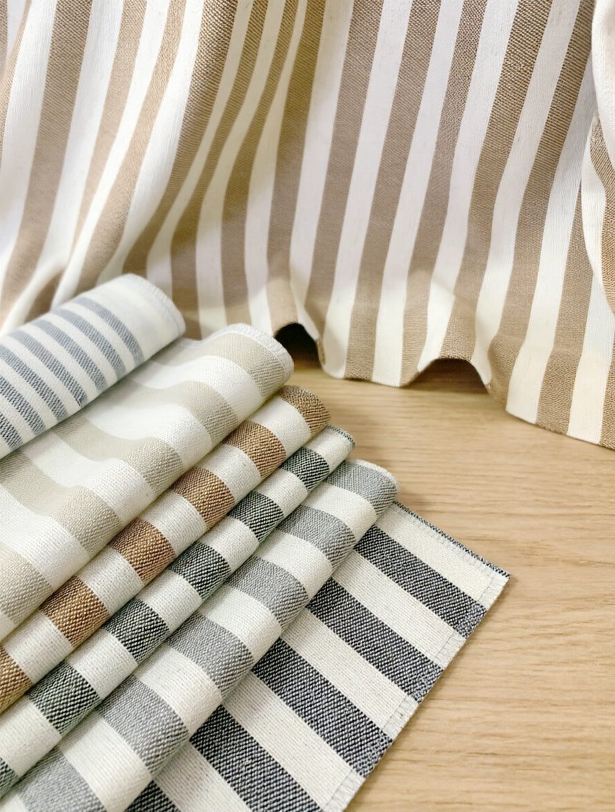 Striped Roman Shades in woven neutral fabric with vertical beige and white stripes, beside layered gray and taupe swatches
