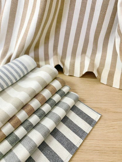 Striped Roman Shades in woven neutral fabric with vertical beige and white stripes, beside layered gray and taupe swatches
