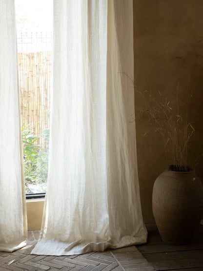 Ivory white linen curtains hanging in a sunlit living room, showcasing soft natural fabric texture and elegant drape