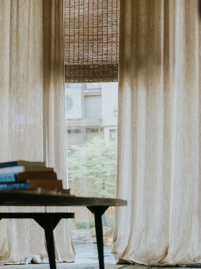 Woven Roman Shades in natural jute with a warm cinnamon tone and textured woven detail beside sheer curtains